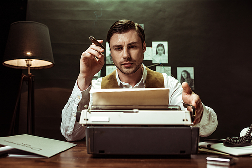 Serious detective with cigar using typewriter in dark office