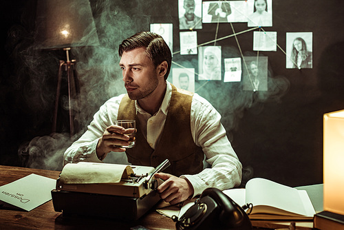 Detective holding glass of cognac while using typewriter in dark office