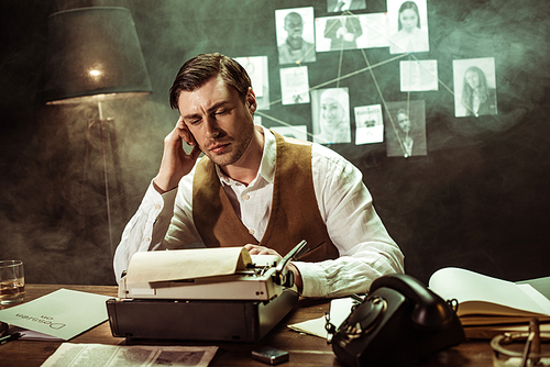 Pensive detective in white shirt sitting at table with typewriter in dark office