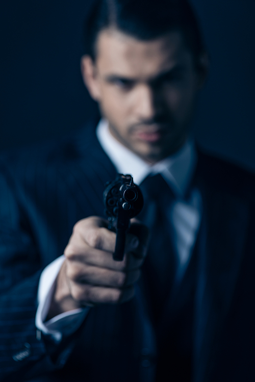 Selective focus of gangster aiming gun and  on dark background