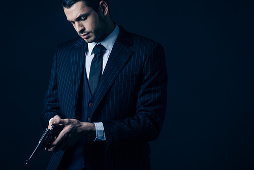 Gangster in elegant suit loading revolver on black background