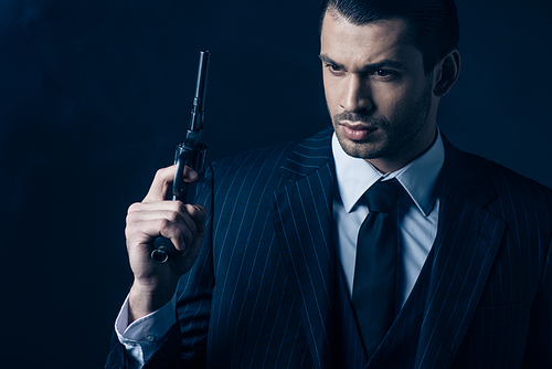 Pensive gangster raising gun on dark blue background