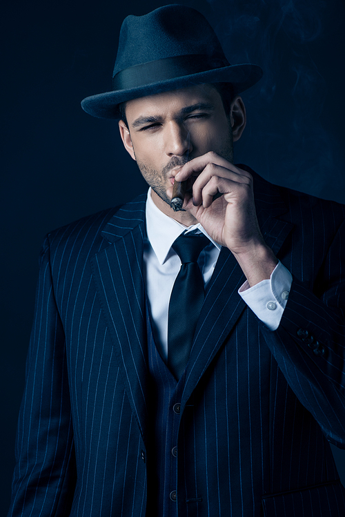 Front view of mafioso smoking cigar on dark background