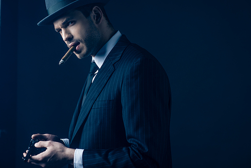 Gangster with cigar in mouth loading gun on dark blue background