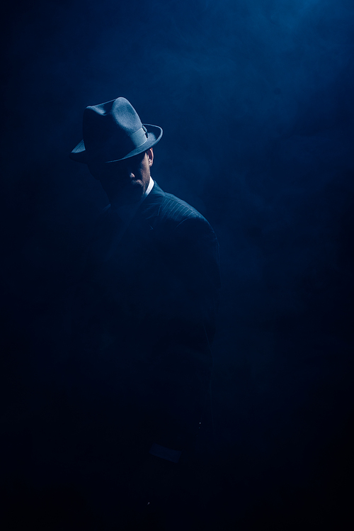 Silhouette of mafioso in suit and felt hat on dark blue background