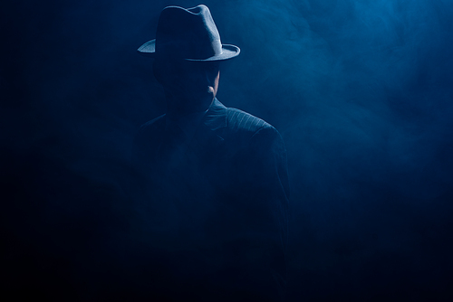 Silhouette of mafioso in felt hat and suit on dark background