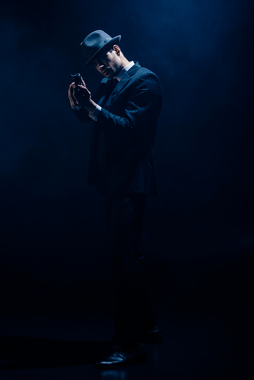 Gangster with clenched hands aiming weapon on dark blue background