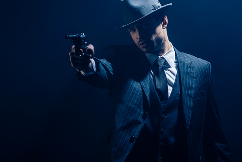 Gangster aiming weapon with outstretched hand on dark background