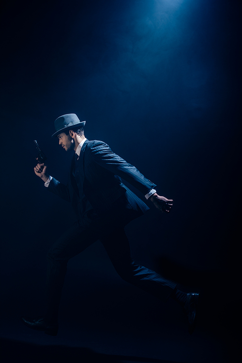 Gangster raising hand with gun and running on dark blue background