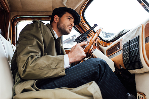 Low angle view of mafioso holding gun and driving car