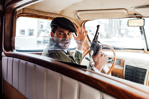 Selective focus of irritated gangster with gun looking back in car