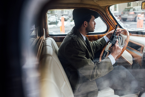 Selective focus of gangster holding weapon and steering wheel in car