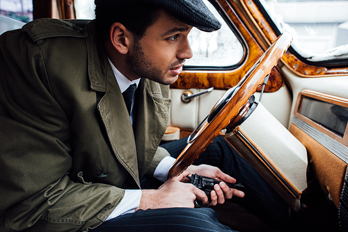 Selective focus of mafioso with gun in ambush sitting in car