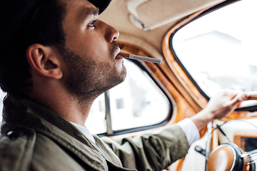 Selective focus of mafioso smoking and holding steering wheel in car