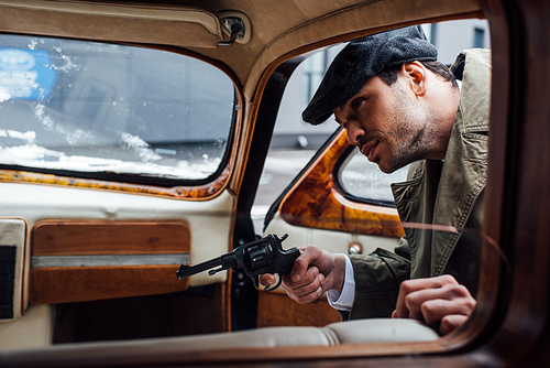 Selective focus of mafioso aiming gun and looking into retro car