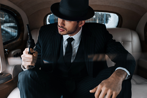 Selective focus of gangster sitting with revolver in retro car