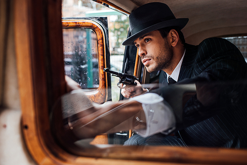 Selective focus of gangster sitting in ambush with gun in retro car