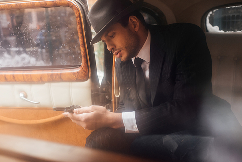 Mafioso looking on revolver in hands while sitting in car