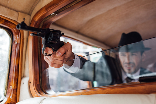 Selective focus of gangster aiming gun with outstretched hand from retro car