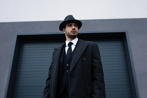 Low angle view of mafioso in black coat and felt hat on street