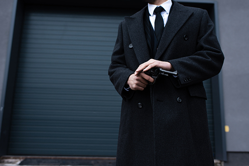 Cropped view of gangster in black coat holding revolver on street