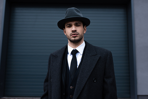 Front view of mafioso in black coat and felt hat on street