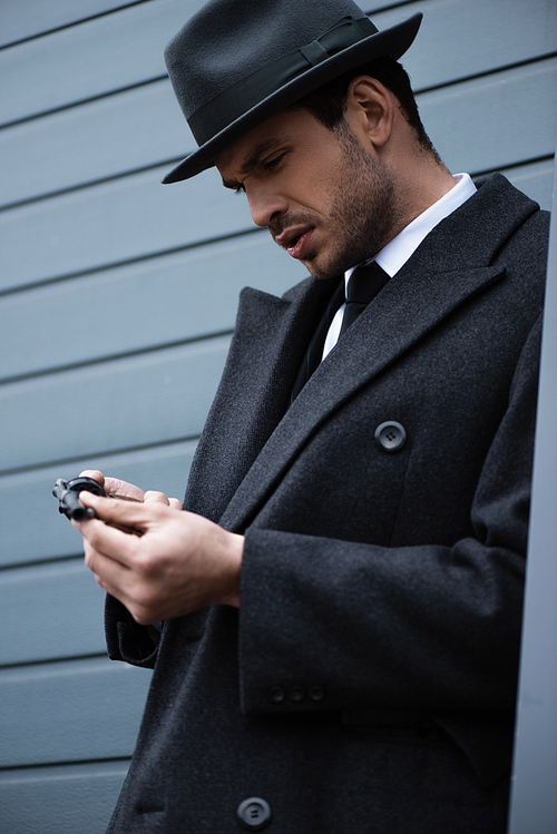 Mafioso concentrated on gun in hands near wall on street