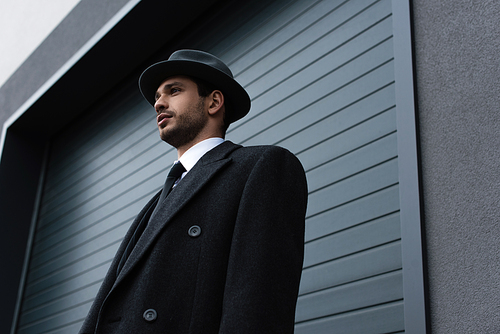 Low angle view of elegant mafioso near wall on street