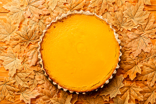 top view of pumpkin pie with autumnal foliage on wooden background