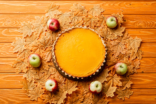 top view of thanksgiving pumpkin pie with apples and autumnal foliage on wooden background