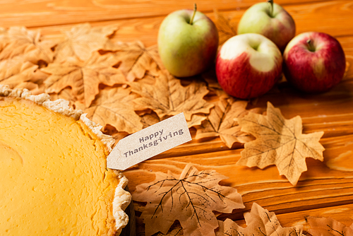 selective focus of thanksgiving pumpkin pie with apples and autumnal foliage on wooden background