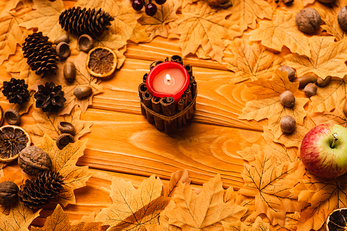 burning candle with autumnal decoration on wooden background