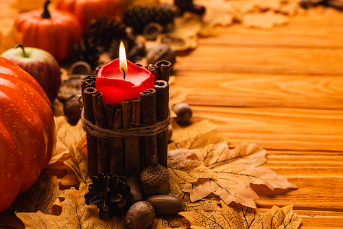 selective focus of burning candle with autumnal decoration on wooden background