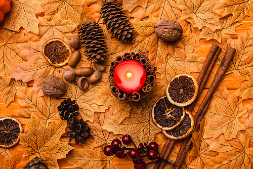 top view of burning candle with autumnal brown decoration on golden foliage