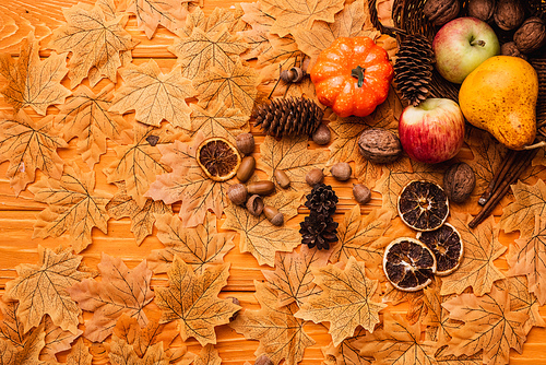 top view of autumnal decoration and food scattered from wicker basket on golden foliage on wooden background