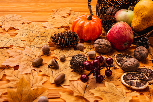 autumnal decoration and food scattered from wicker basket on golden foliage on wooden background