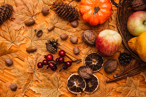 top view of autumnal decoration and food scattered from wicker basket on golden foliage on wooden background