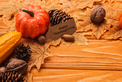 corn, pumpkin, autumnal decoration and happy thanksgiving card on wooden background