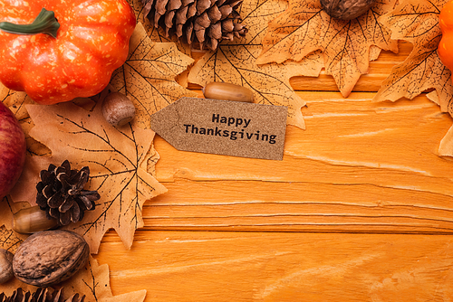 top view of pumpkin, autumnal decoration and happy thanksgiving card on wooden background