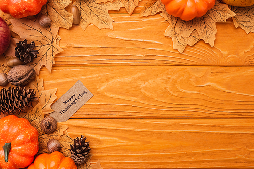 top view of pumpkins, autumnal decoration and happy thanksgiving card on wooden background