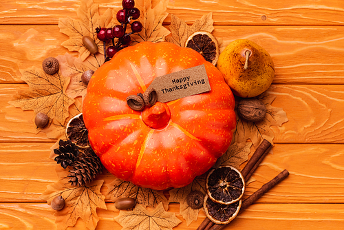 top view of pumpkin with autumnal decoration and happy thanksgiving card on wooden background