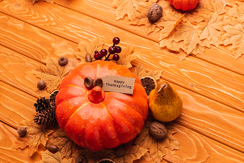 top view of pumpkin with autumnal decoration and happy thanksgiving card on wooden background