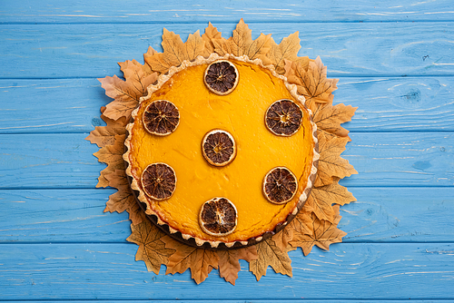 top view of decorated pumpkin pie with golden foliage on blue wooden background