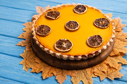 decorated pumpkin pie with golden foliage on blue wooden background