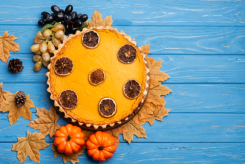 top view of decorated pumpkin pie with golden foliage on blue wooden background