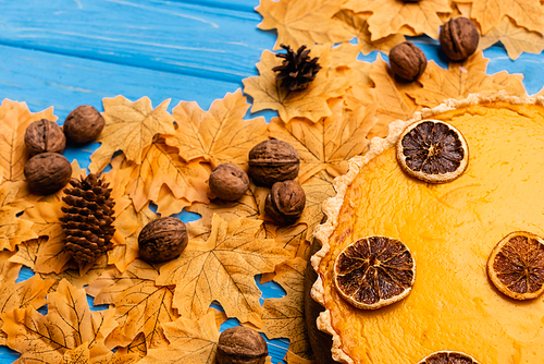 top view of pumpkin pie on autumnal foliage with walnuts and cones