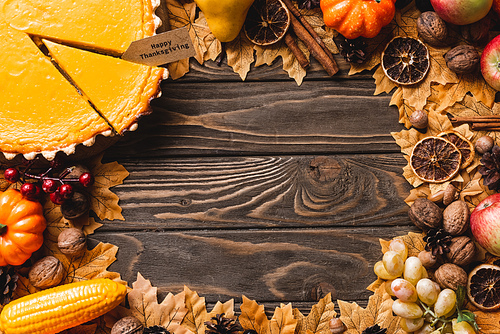 top view of autumnal decoration and pumpkin pie with happy thanksgiving card on brown wooden background