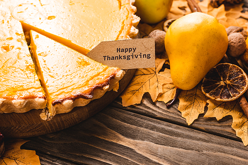 close up view of autumnal decoration and pumpkin pie with happy thanksgiving card on brown wooden background