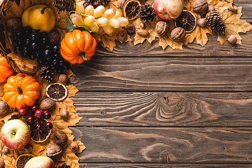top view of autumnal harvest scattered from basket on foliage on brown wooden background