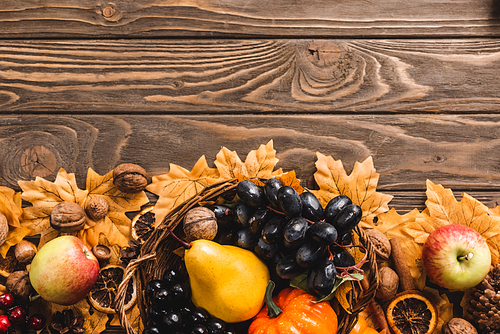 top view of autumnal harvest in basket on foliage on brown wooden background